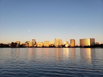 Lake and buildings against clear sky during sunset