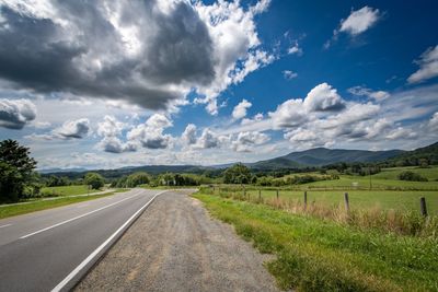 Empty road amidst field against sky