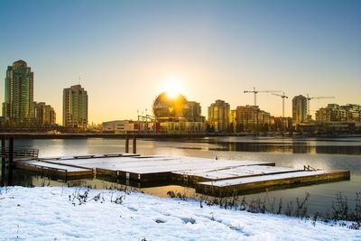 City by frozen lake against clear sky during sunset