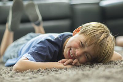 Portrait of smiling boy lying down on carpet at home