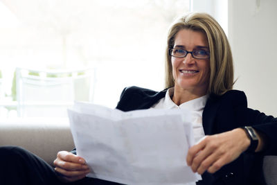 Portrait of confident businesswoman holding documents while sitting on sofa