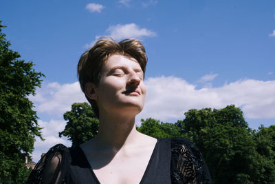 Smiling non-binary person enjoying sunlight under cloudy sky