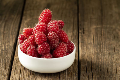 Fresh ripe raspberries in a white ceramic bowl on a dark brown wooden table with space for text