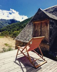 Wooden chairs and table on building by mountain against sky