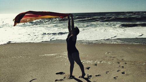 Full length of woman holding scarf while standing at beach against sky