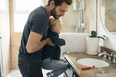 Side view of father carrying daughter at sink in bathroom