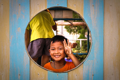 Portrait of happy boy gesturing seen through play equipment