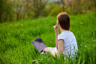 Side view of woman using laptop while sitting on field