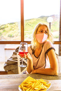 Smiling woman wearing mask holding wineglass sitting at restaurant