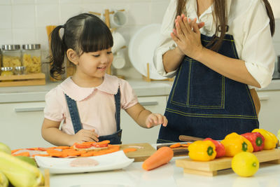 Siblings standing on cutting board in kitchen