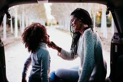 Smiling mother sitting with daughter in car trunk