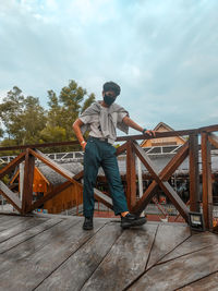 Full length of man wearing mask standing by railing against sky