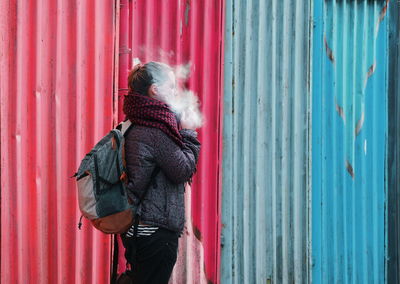 Side view of young woman smoking against metal sheets