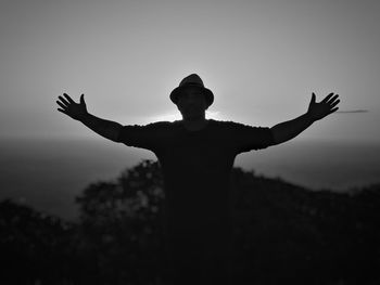 Man with arms outstretched standing against sky