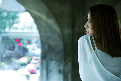 Young woman looking away while standing under bridge