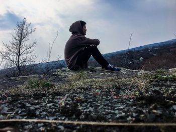 Side view of thoughtful young man with arms crossed sitting on rock