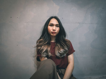 Portrait of beautiful woman sitting against wall