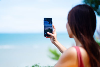 Rear view of woman photographing mobile phone against sky