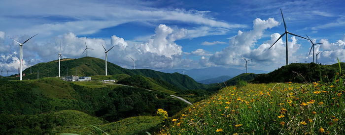 Panoramic view of wind turbines on field against sky