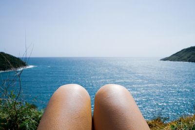 Low section of man relaxing in sea against clear sky