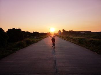 Man walking on road against sky during sunset