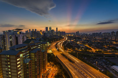 High angle view of illuminated street amidst buildings against sky during sunset