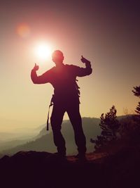 Happy man gesture of triumph. funny hiker on peak in saxony park watch into camera, sun behind head