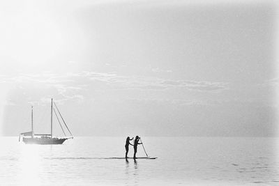 Scenic view of sea against sky with silhouette of couple doing paddleboarding