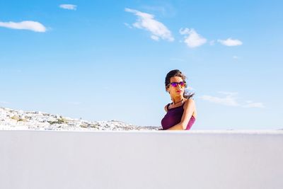 Young woman wearing sunglasses by wall against sky