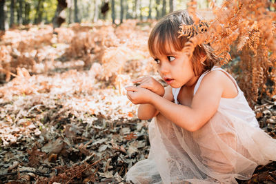 Side view of girl crouching amidst plants on field