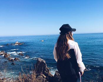 Rear view of woman standing by sea against clear sky