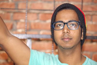 Portrait of young man wearing eyeglasses and knit hat against brick wall