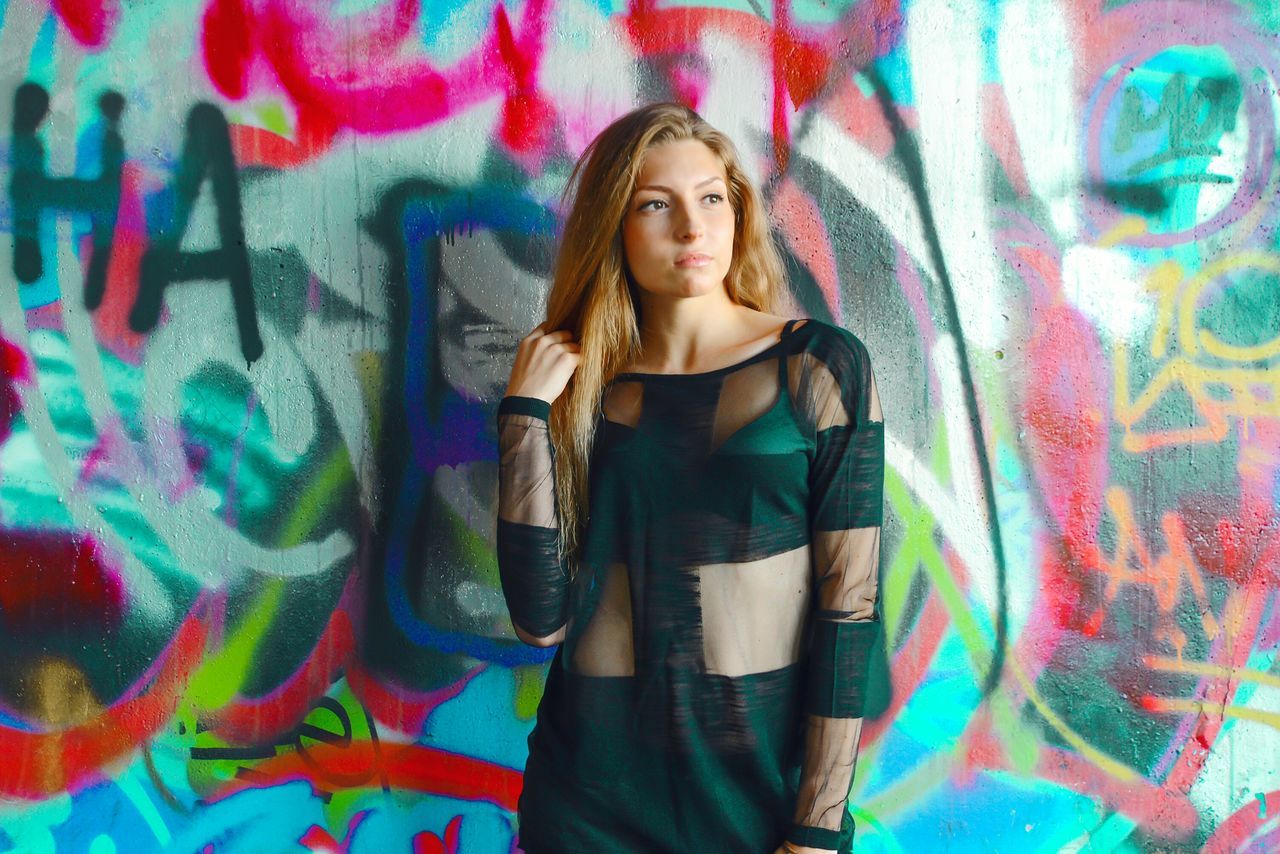 young adult, lifestyles, indoors, looking at camera, casual clothing, front view, leisure activity, portrait, graffiti, young women, wall - building feature, person, standing, art, multi colored, fashion, creativity, art and craft