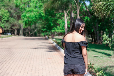 Rear view of young woman standing against trees at park