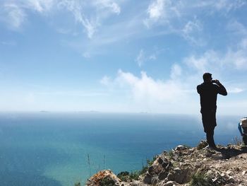 Rear view of man standing on rock against sky