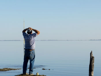 Man fishing in sea against clear blue sky