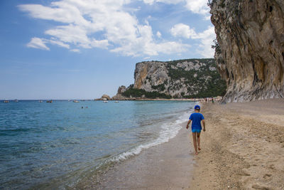 Rear view of men on beach against sky