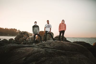 People standing on rock by sea against clear sky