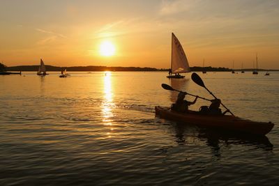 People kayaking in lake during sunset