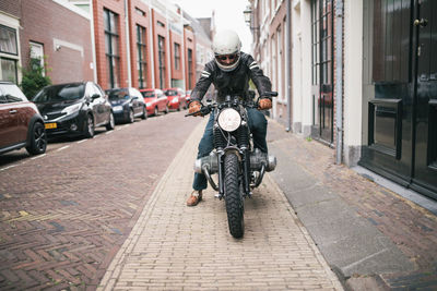 Full length of man riding motorcycle on street in city