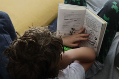 High angle view of boy reading book while relaxing on bed