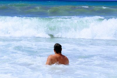Rear view of shirtless man swimming in sea