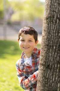 Portrait of smiling boy standing by tree trunk in park