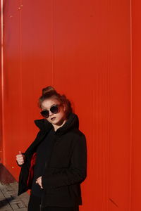 Portrait of young woman standing against red wall