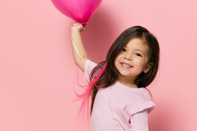 Portrait of smiling young woman with balloons against pink background