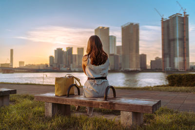 Full length rear view of woman looking at city against sky during sunset