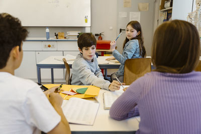 Boy taking pencil from female friend sitting at desk in classroom