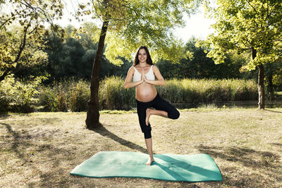 Portrait of pregnant woman doing yoga on field against trees