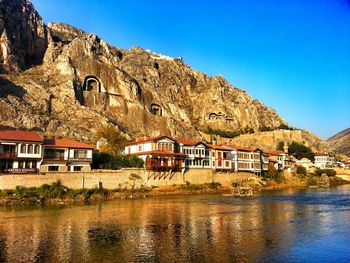 Houses by river in town against clear blue sky