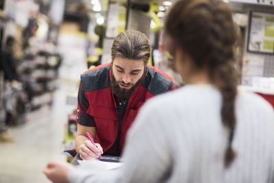 Salesman writing on document while female customer standing in hardware store